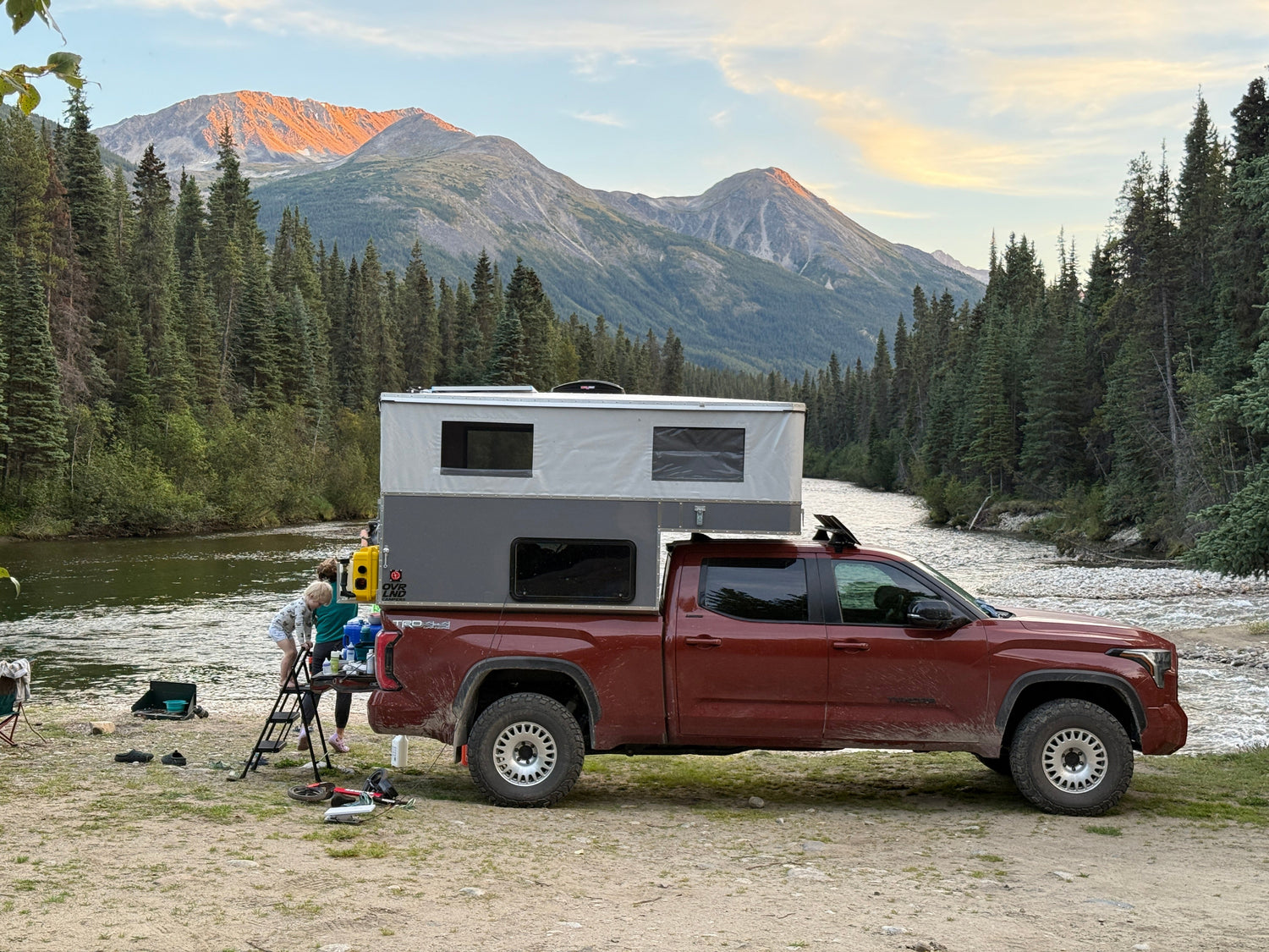 Tundra with an OVRLND camper shell parked by a lake with mountains in the background