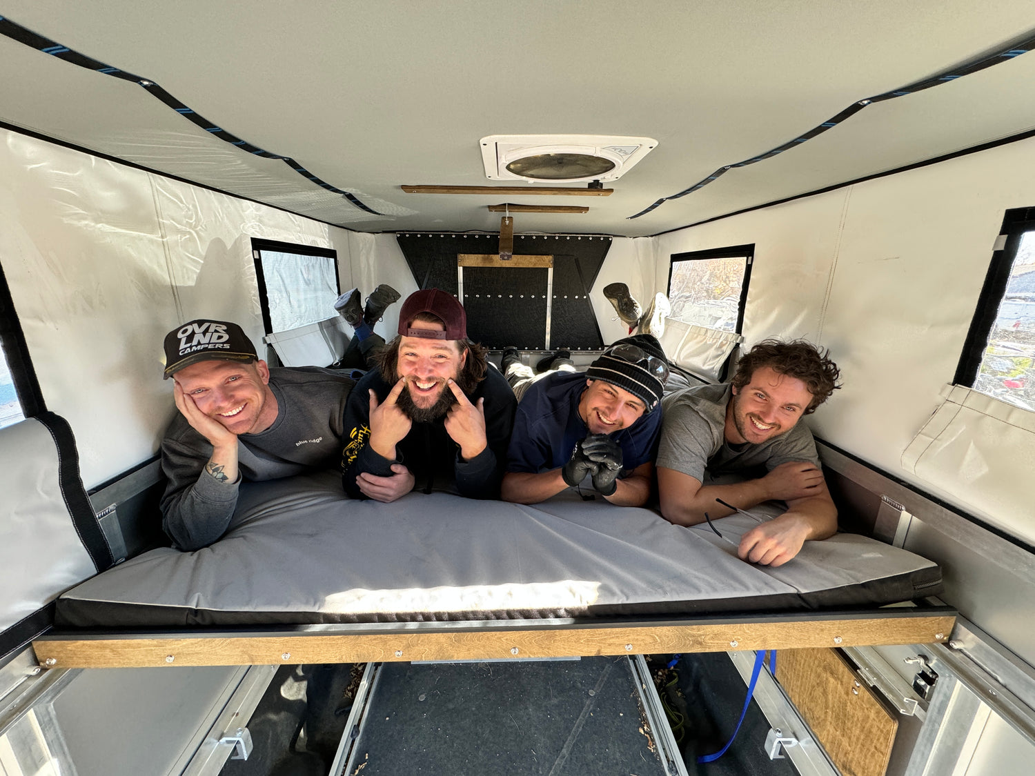 4 people laying in the bed of an OVRLND Pop-Top Camper shell on a Ram 2500