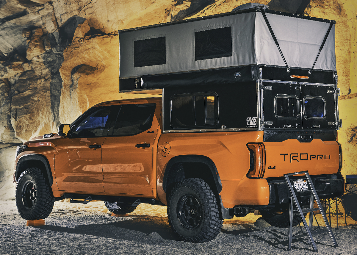 Orange truck with a pop top camper parked in front of rocky cliffs